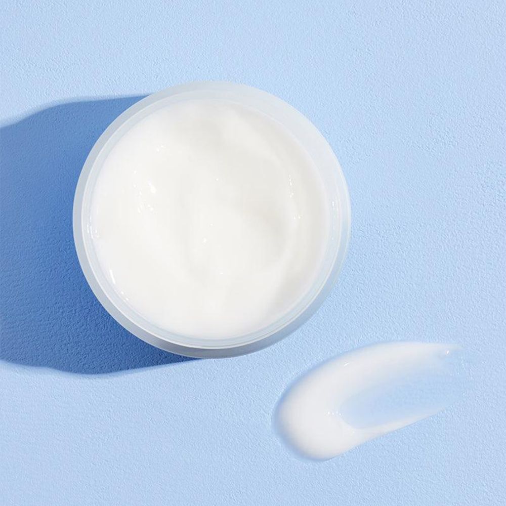 Un pot blanc ouvert avec une crème blanche et une touche de crème à côté sur fond bleu.