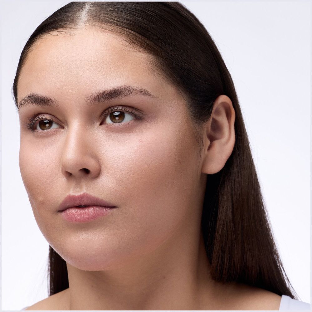 Portrait d'une femme aux cheveux bruns. Elle regarde sur le côté. Son visage est lisse.