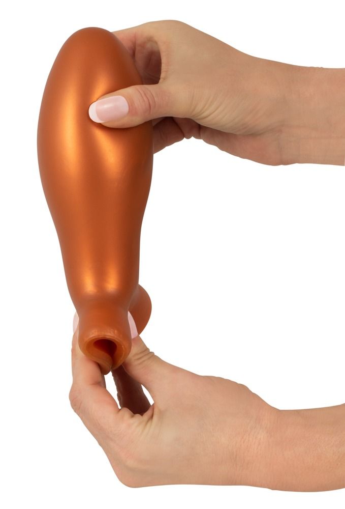 Mains étirant l'ouverture d'un plug anal orange.