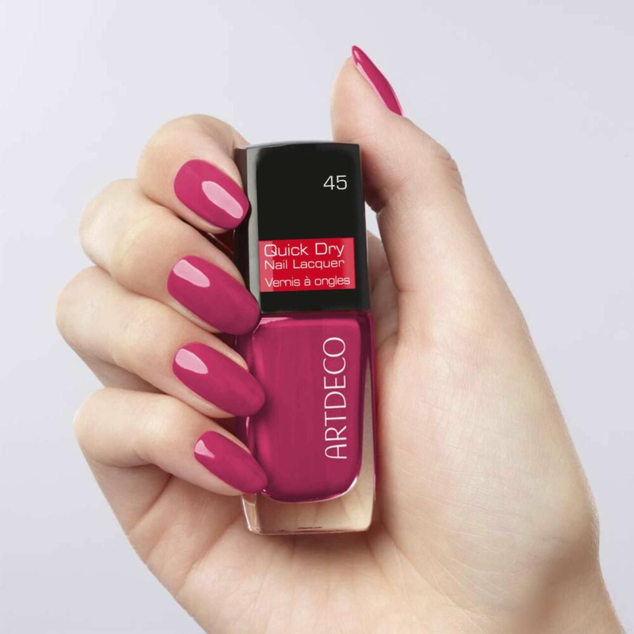 Hand houdt nagellakfles vast. Geverfde nagels in rood. Merk Artdeco. Kleurnummer 45.