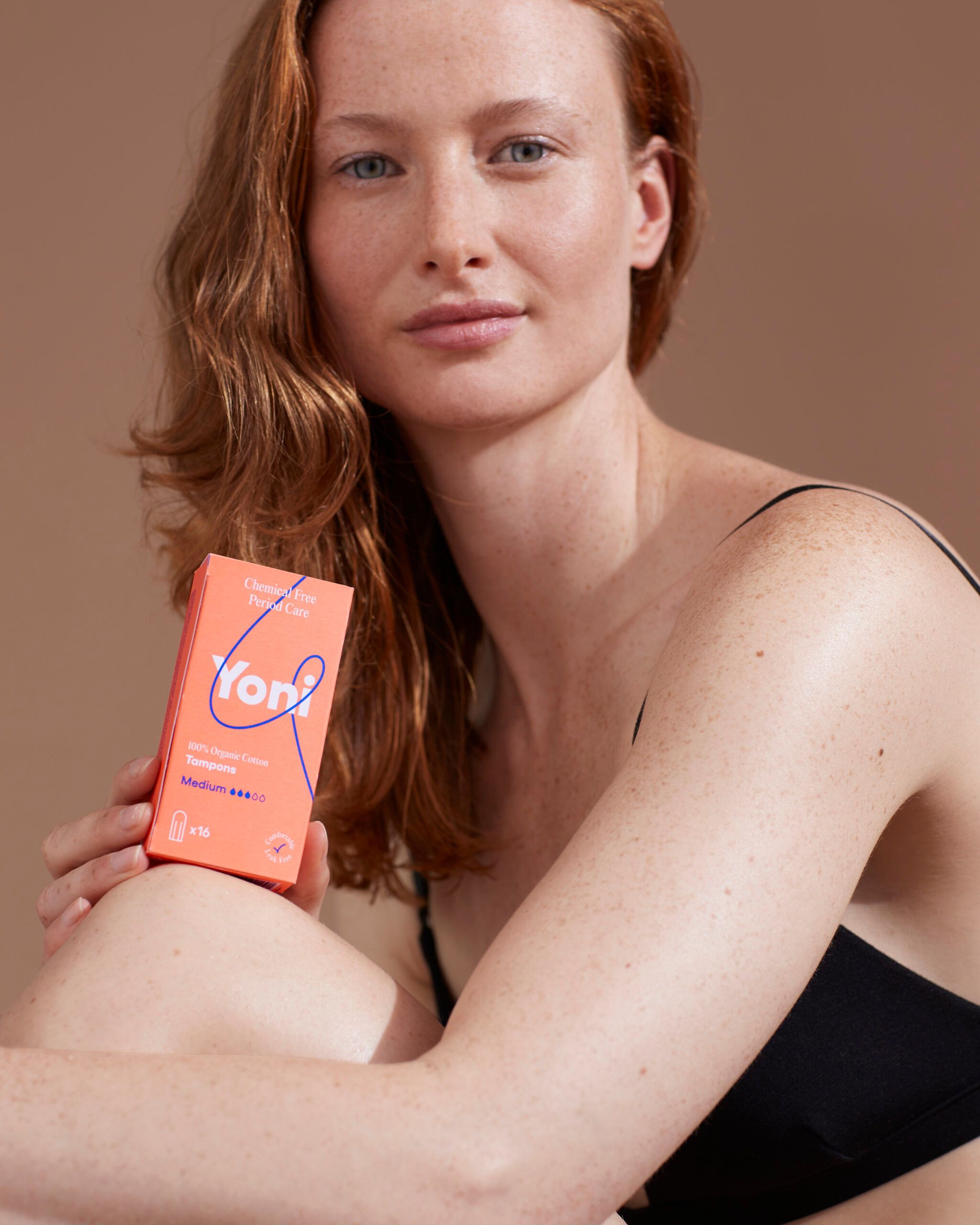 Une femme tient une boîte orange de tampons. Le mot "Yoni" est visible.