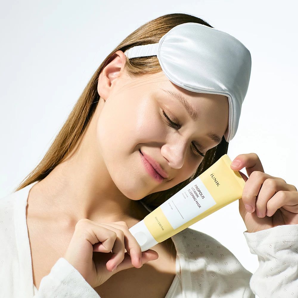 Vrouw met slaapmasker houdt een gele tube Propolis Vitamin Sleeping Mask vast.