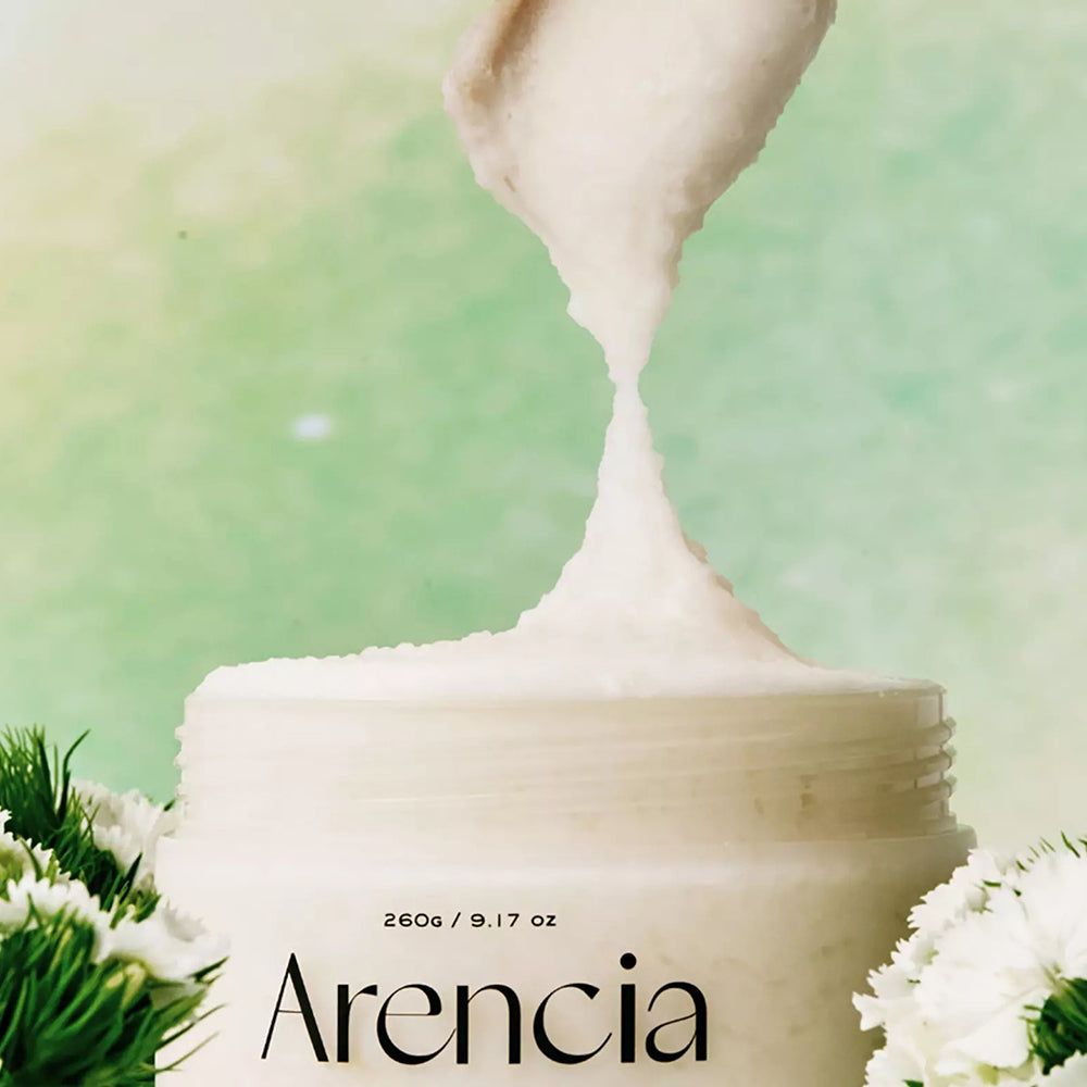 ARENCIA scrub uit een witte pot gehaald. Lichte textuur, omringd door witte bloemen.