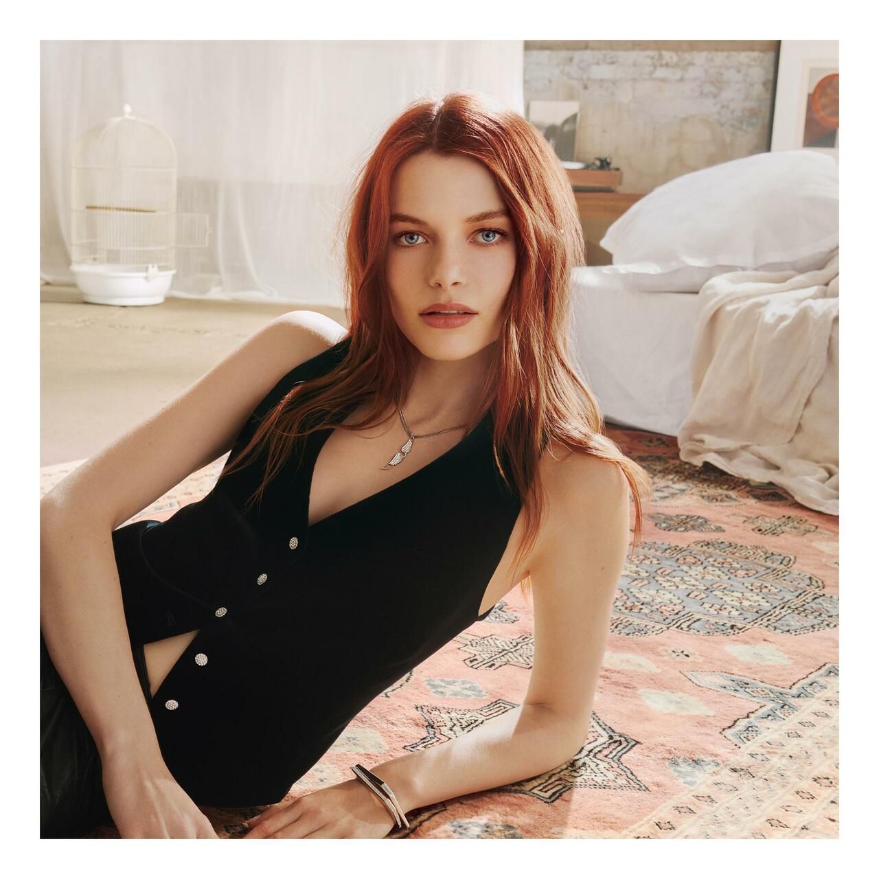 Femme aux cheveux roux allongée sur un tapis, portant un gilet noir.