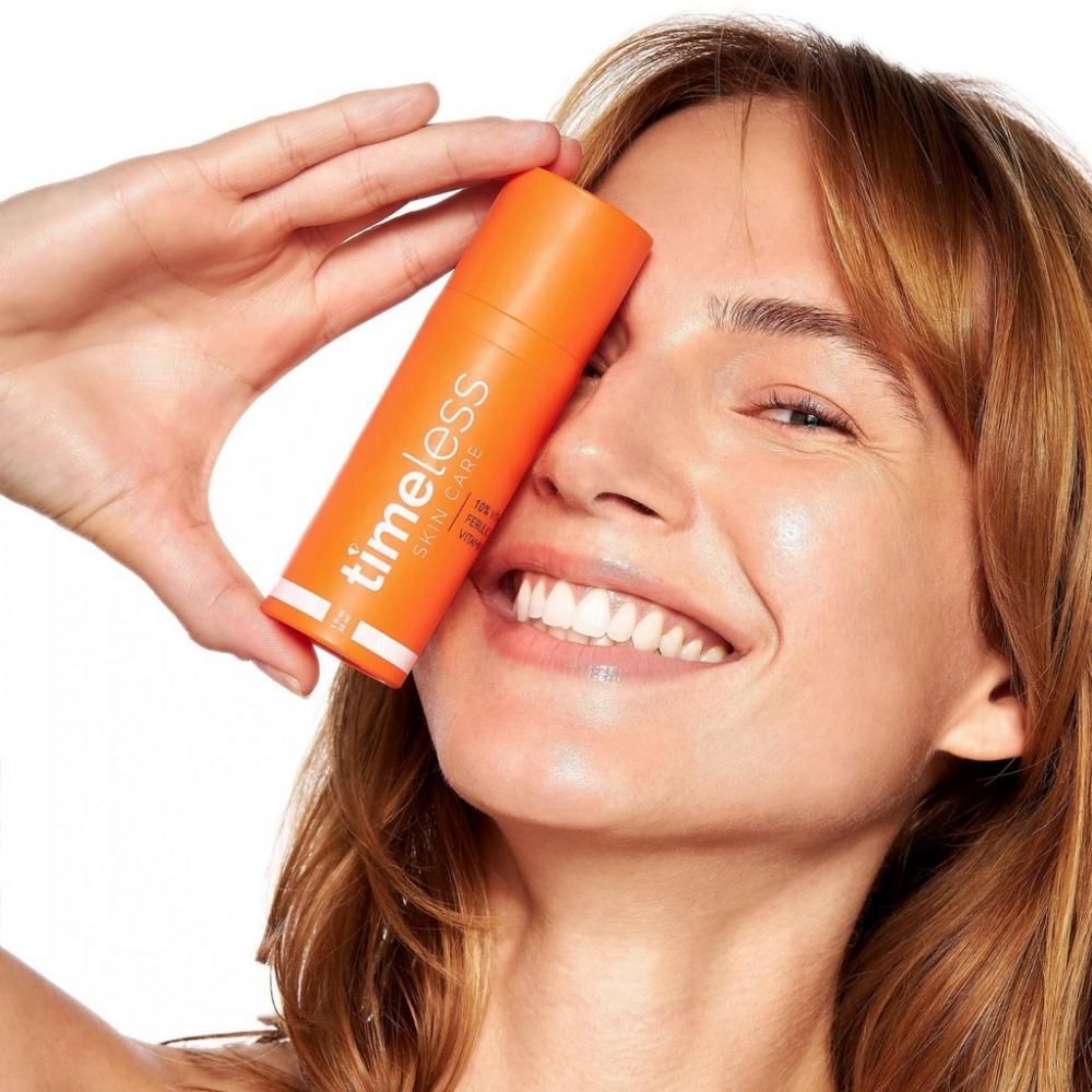 Femme tenant un flacon orange. Inscription : Timeless Skin Care. Produit : 10% vitamine C, acide férulique, vitamine E.