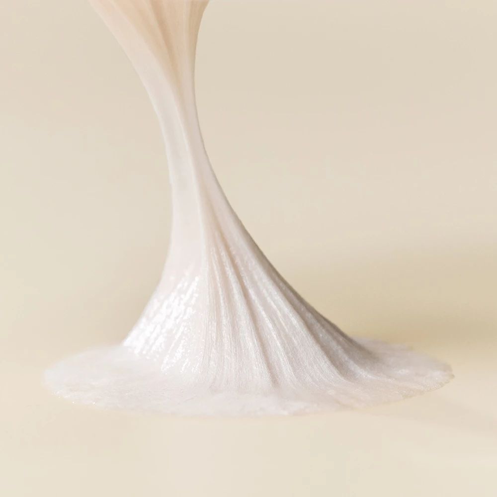 Gros plan sur un filet de mousse nettoyante blanche qui s'étale sur une surface.