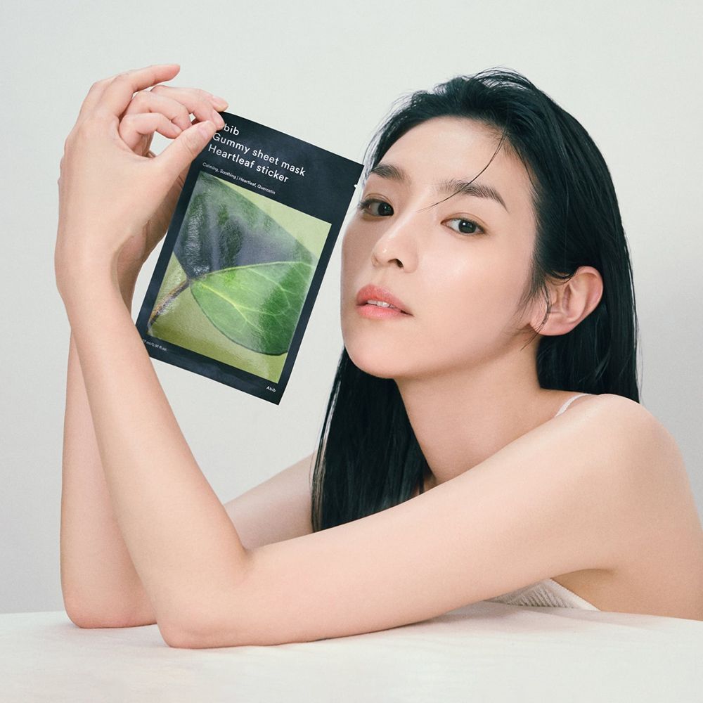 Vrouw houdt zwarte verpakking met productnaam en bladmotief vast. Tekst: ABIB Gummy Sheet Mask Heartleaf sticker.