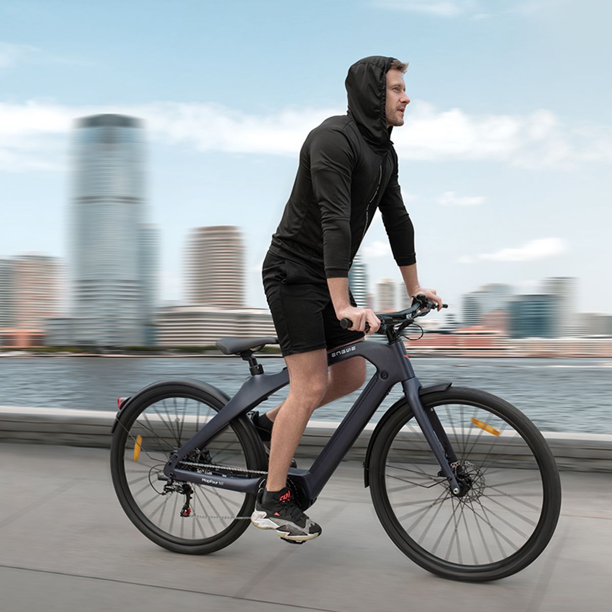 Personne faisant du vélo électrique gris foncé. Paysage urbain en arrière-plan. Logo Engwe.