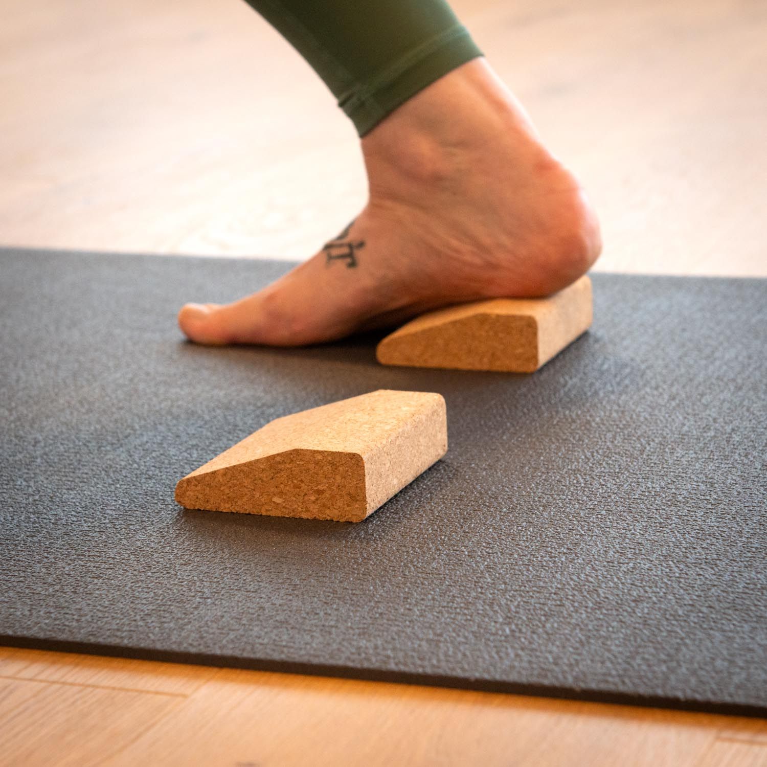 Voet op kurken wig, op yogamat. Tweede wig ernaast. Lichte houten achtergrond.