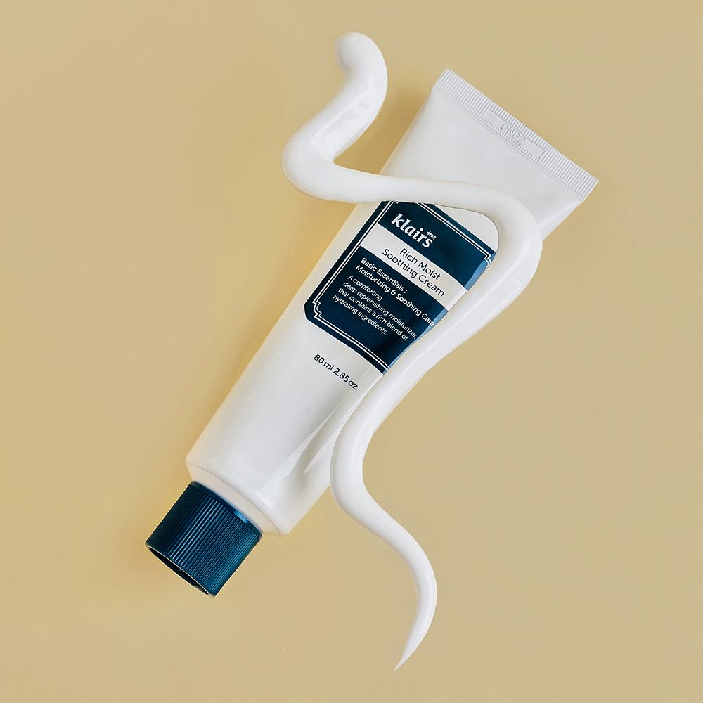 Klairs Rich Moist Soothing Cream tube omgeven door een slang van witte crème.