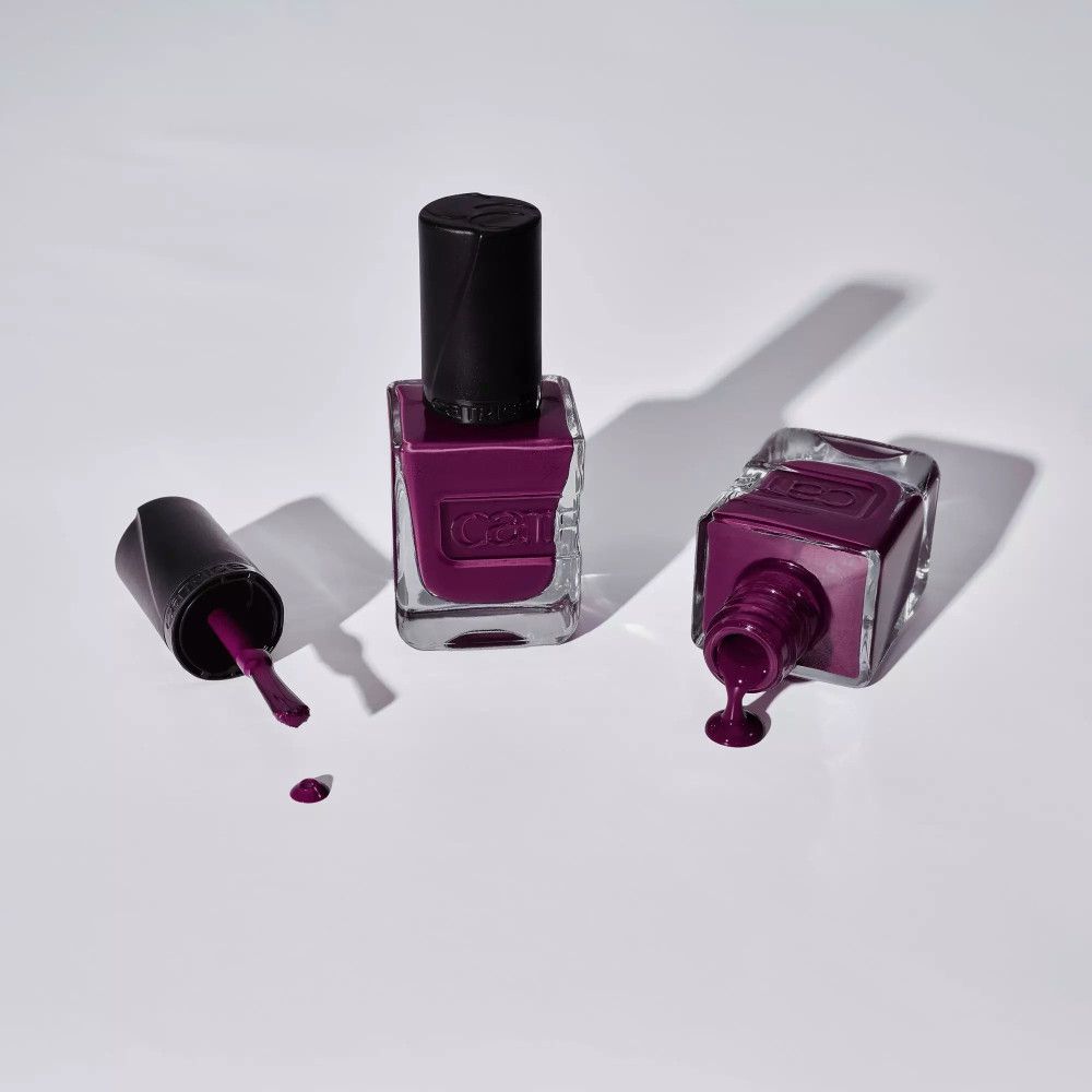Trois flacons de vernis à ongles. Vernis violet foncé. Bouchons noirs. Sur fond clair. Vernis renversé.