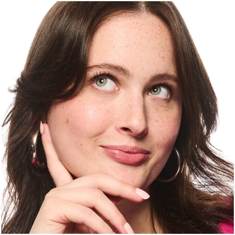 Portrait d'une femme rousse regardant vers le haut. Elle porte des boucles d'oreilles et a la main sur le menton.