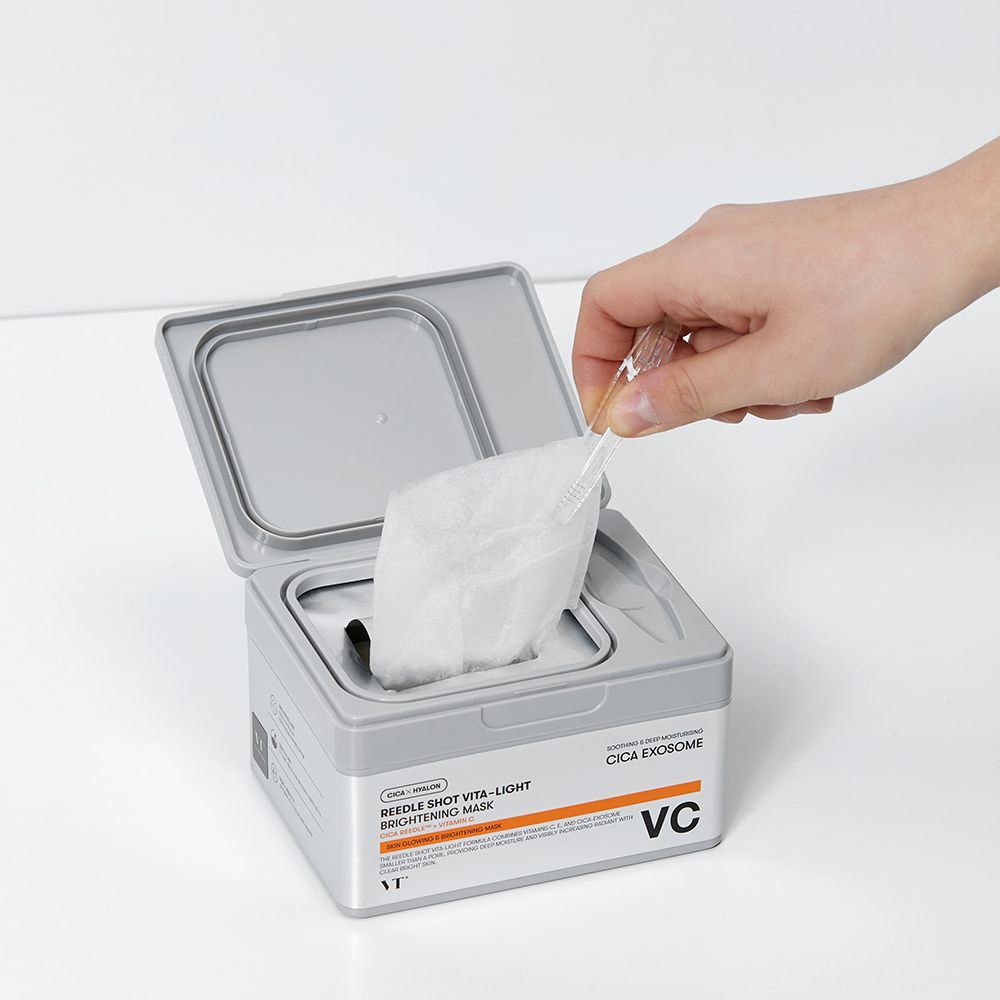 Main retirant un masque éclaircissant Cica Care Vita-Light de la boîte ouverte.
