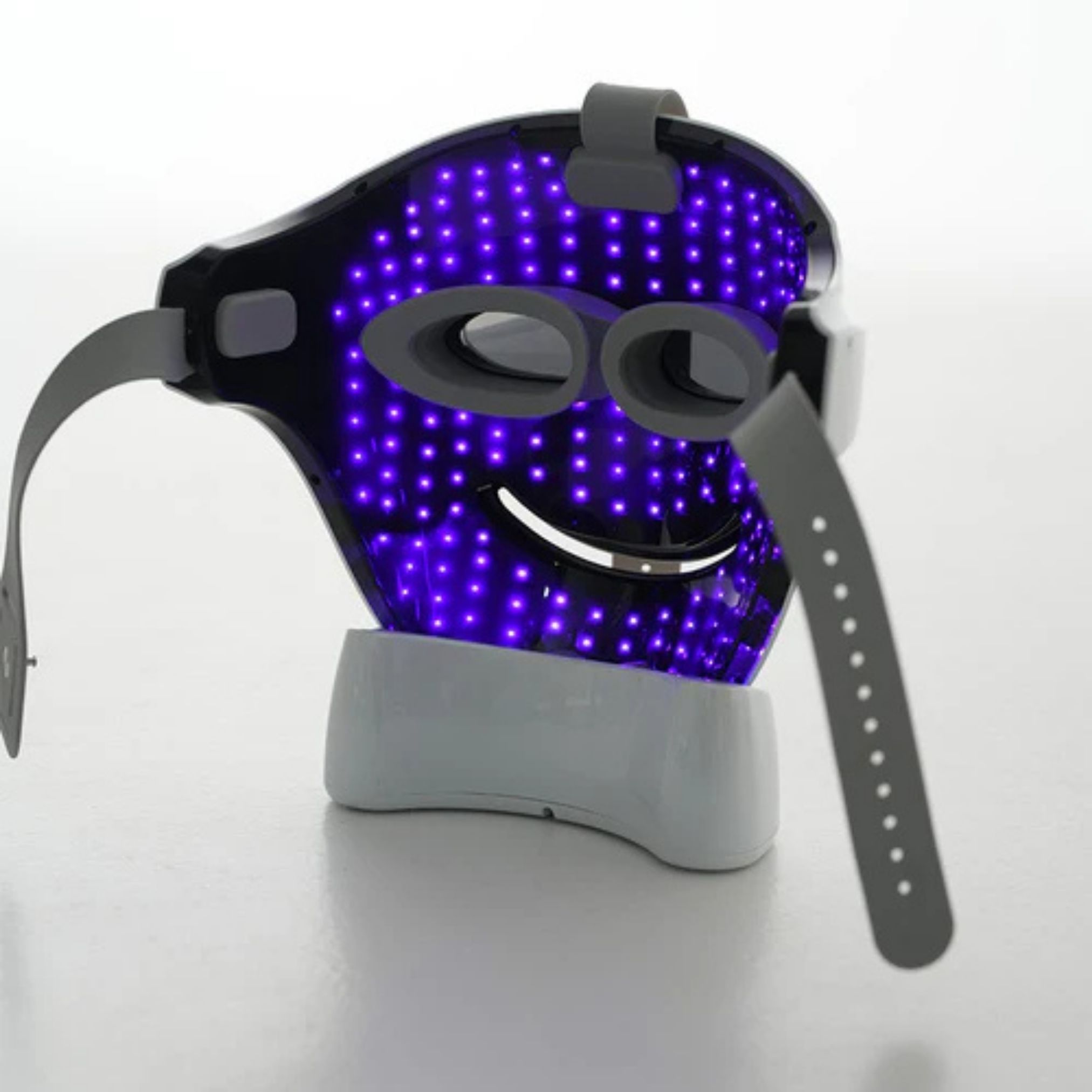 Gezichtsmasker met paarse LED's. Grijze bandjes en houder. Masker op witte basis.