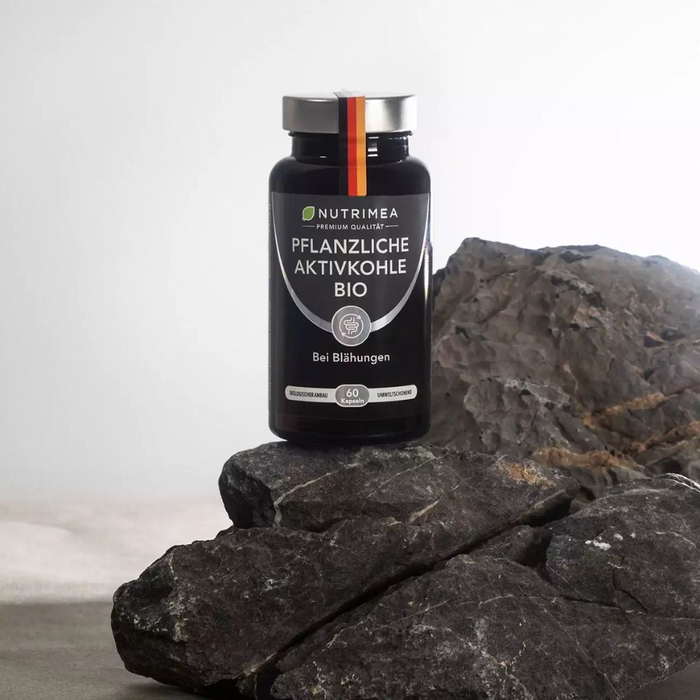 Zwarte fles met capsules op steen. Opschrift: Plantaardige Actieve Kool BIO. 60 capsules.