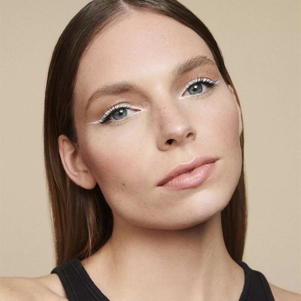 Gros plan d'un visage avec eye-liner blanc. Les lèvres sont légèrement teintées.