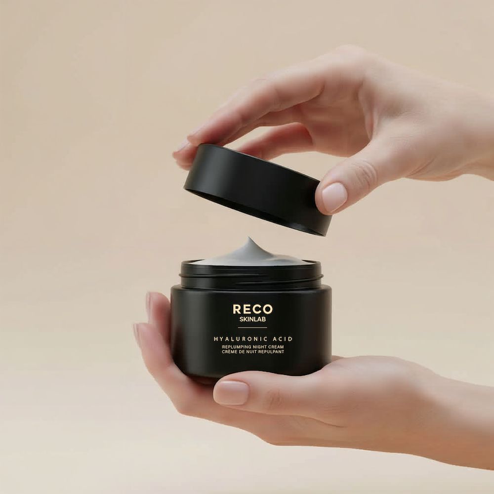 Mains tenant un pot noir avec couvercle. Inscription : RECO, Acide Hyaluronique, Crème de nuit repulpante. Le couvercle est ouvert, la crème est visible.