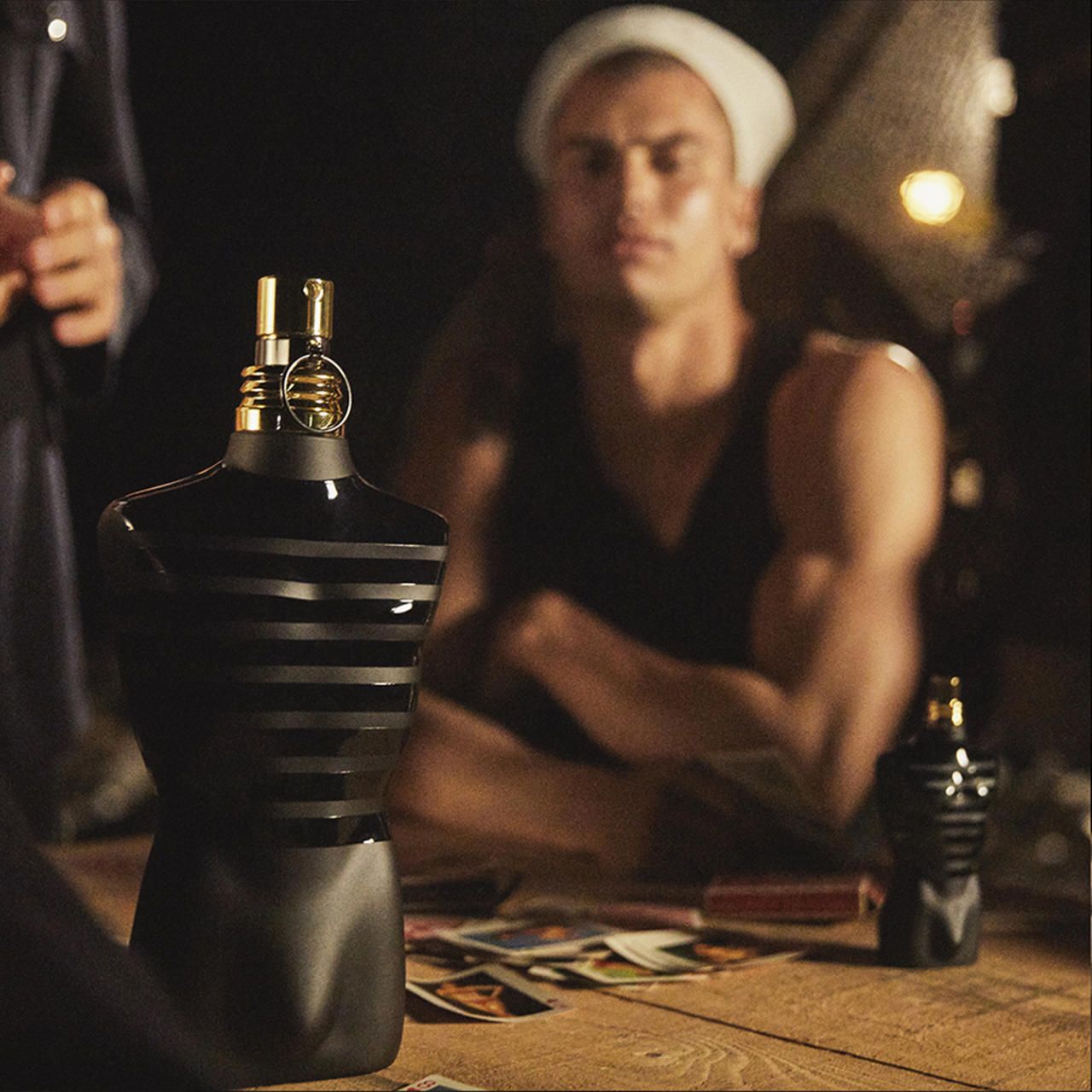Zwarte torso-vormige fles met gouden dop op een tafel. Een persoon op de achtergrond. Geen andere inscriptie.