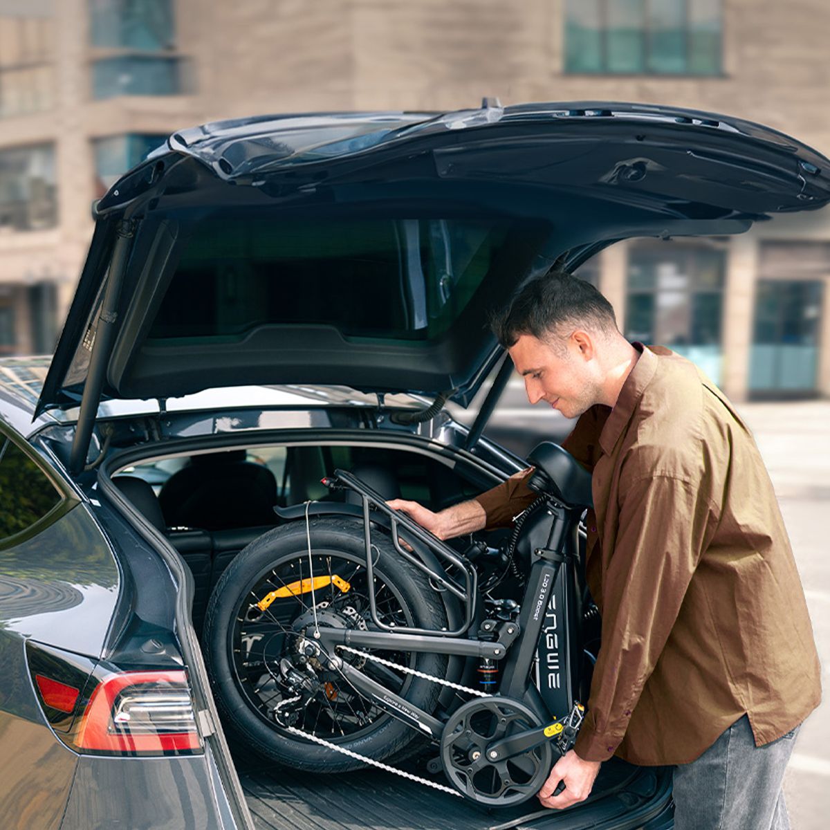 Man haalt een opgevouwen zwarte elektrische fiets uit een auto. Het ENGWE-logo is zichtbaar.