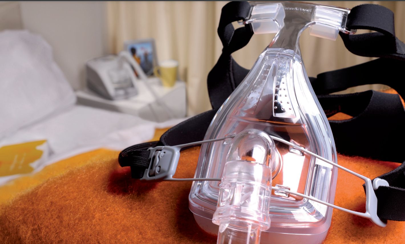 Masque facial complet Fisher & Paykel Forma™ pour la thérapie du sommeil par PPC. Fabriqué en plastique transparent, avec un harnais noir. Conçu pour une utilisation avec les appareils PPC, présenté dans un cadre de chambre à coucher.