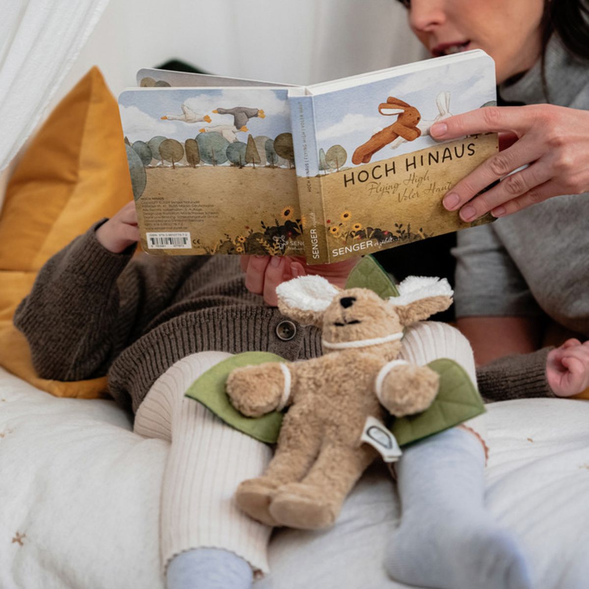 Enfant et mère lisent un livre. Livre avec illustrations de lapins. Titre : Hoch Hinaus. Peluche lapin.