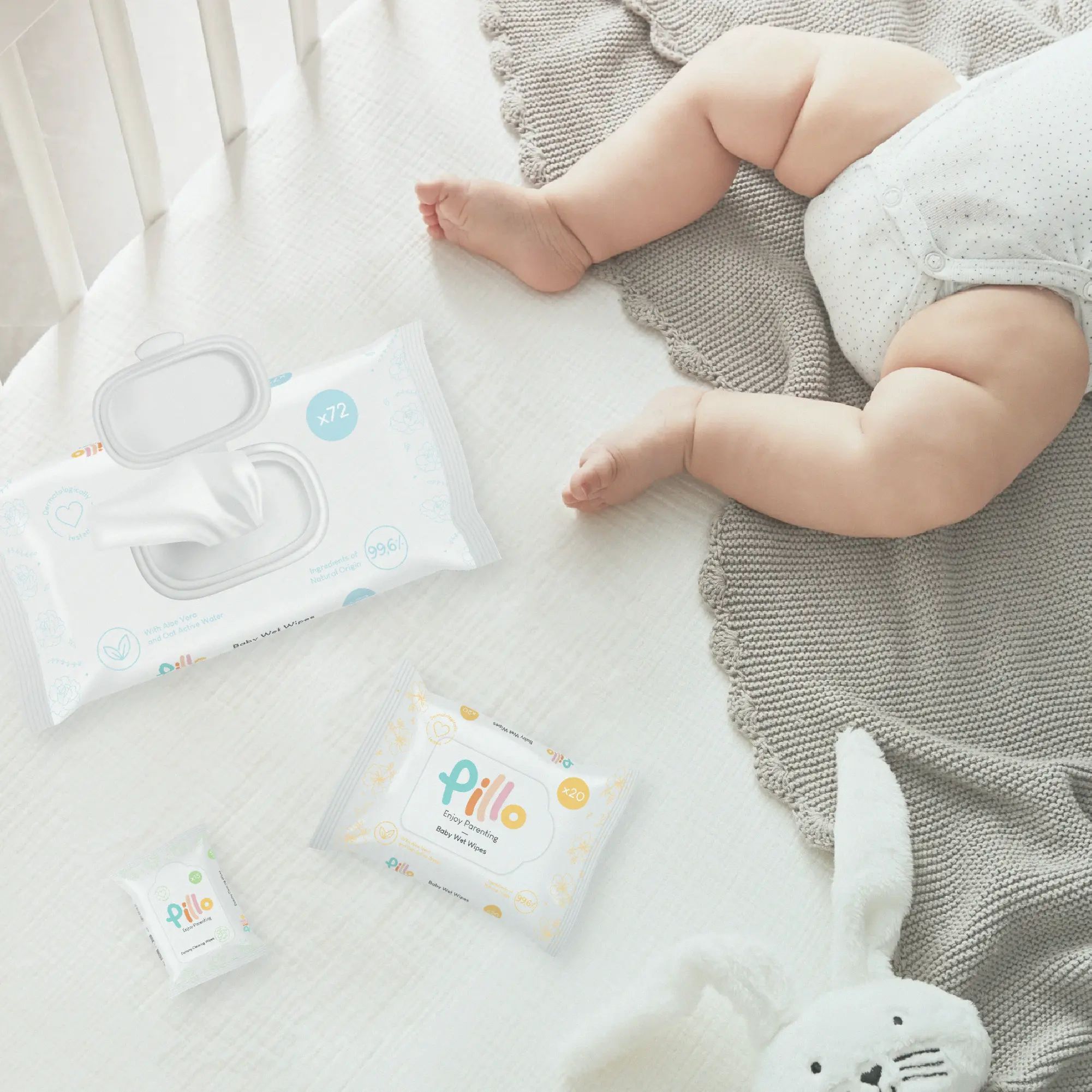 Plusieurs paquets de lingettes Pillo Baby, dont un ouvert, sur une surface blanche. Un bébé est à côté.