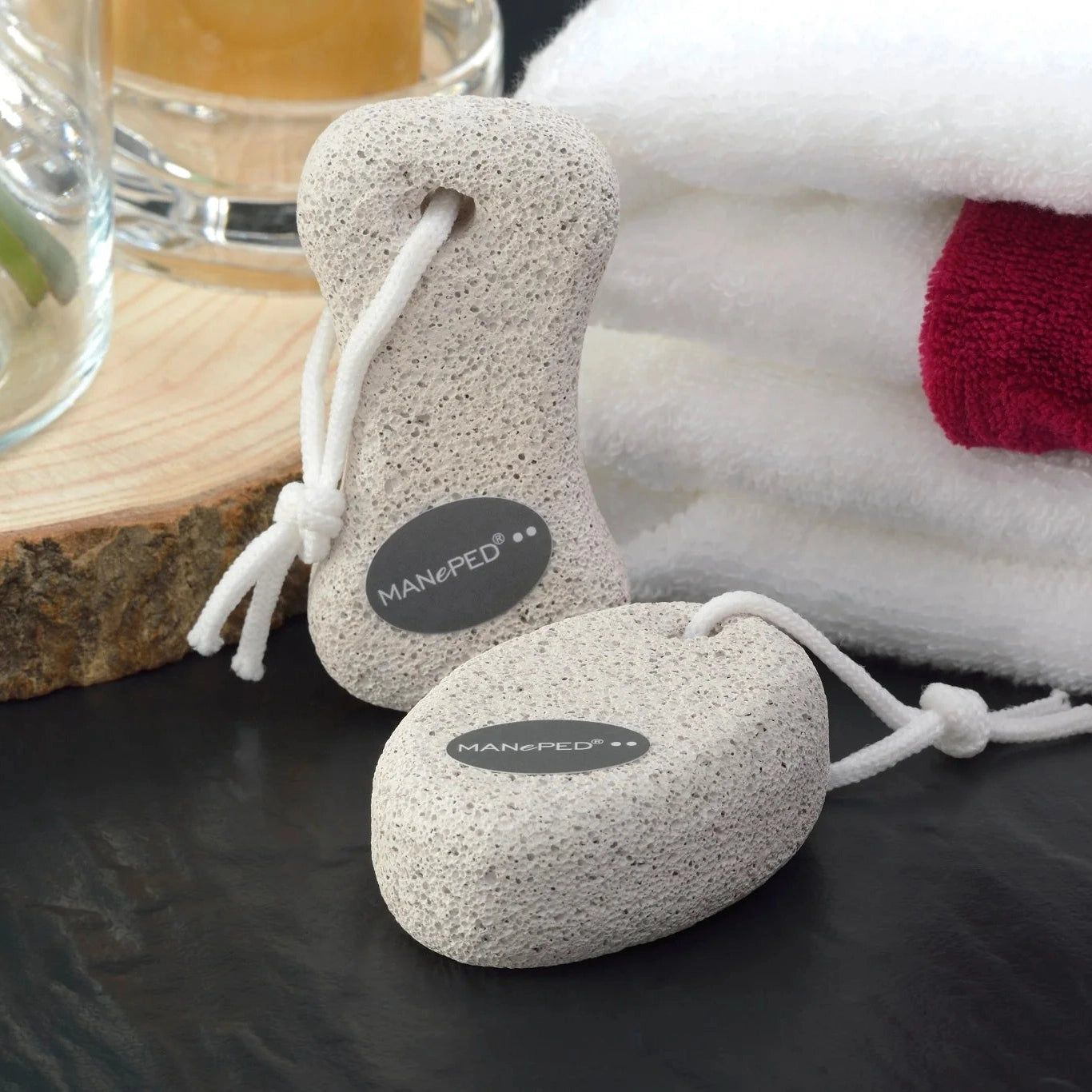 Deux pierres ponces avec cordon blanc. Logo MANePED. Sur fond noir, serviettes en arrière-plan.