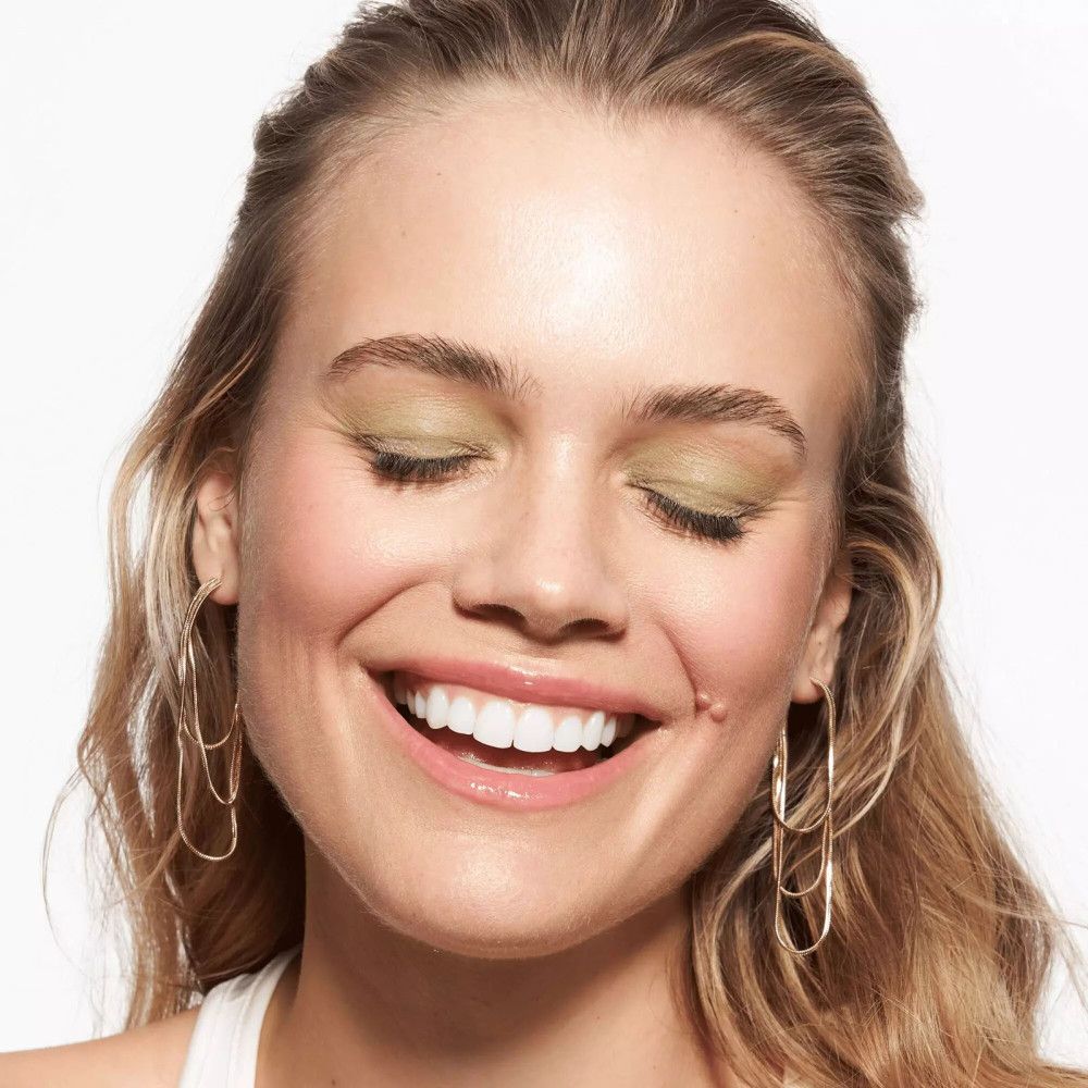 Gros plan d'une femme souriante avec du maquillage et des boucles d'oreilles dorées.