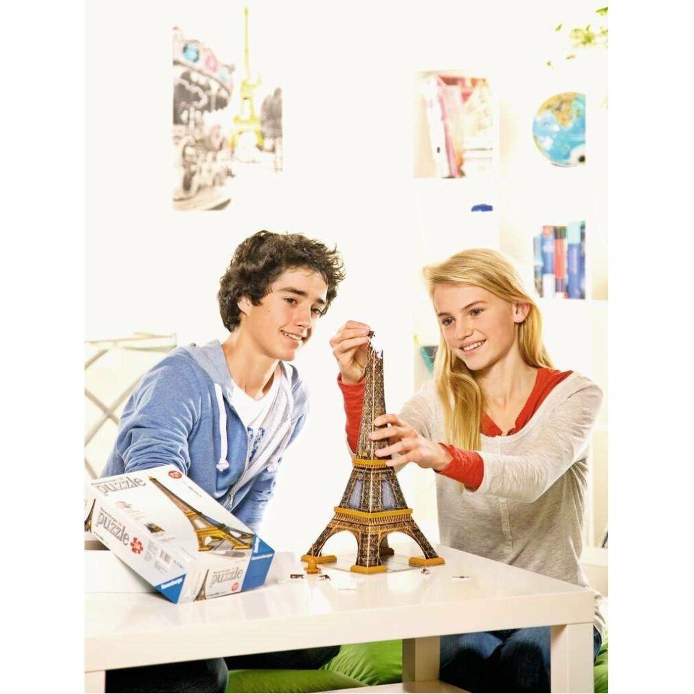 Twee tieners bouwen een 3D-puzzel Eiffeltoren. Puzzel en verpakking op een tafel. Lichte omgeving.