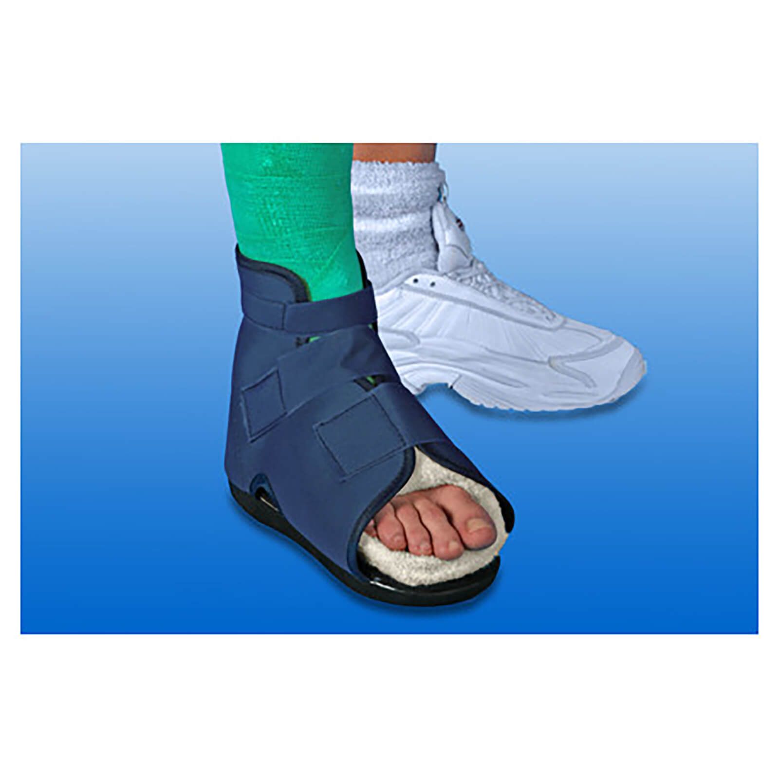 Blauwe loopschoen met klittenbandsluitingen en zachte voering. Voet in groen verband. Op de achtergrond een witte sportschoen.