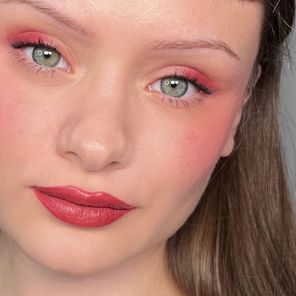 Gros plan d'un visage maquillé. Fard à paupières rouge, blush et rouge à lèvres. Yeux verts.