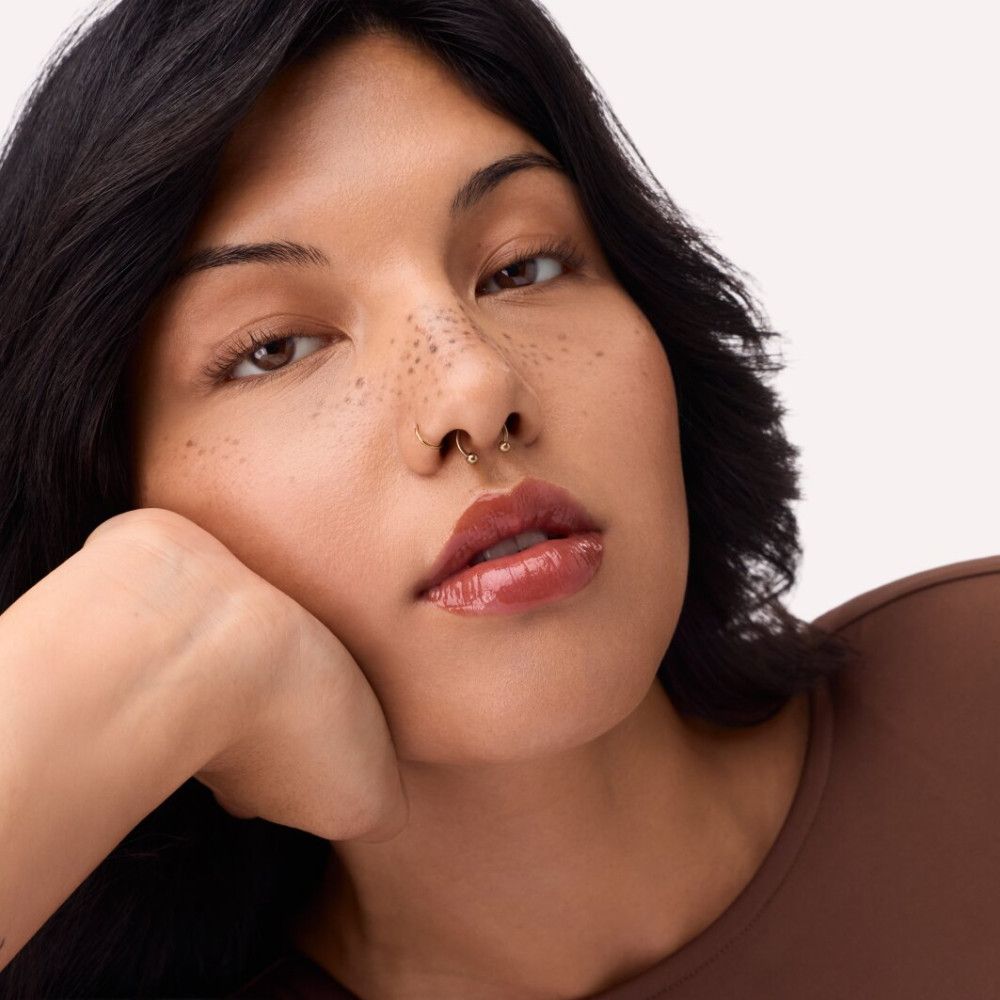 Portret van een vrouw met lipgloss. Kleur: oranje-bruin. Ze steunt haar kin op haar hand.