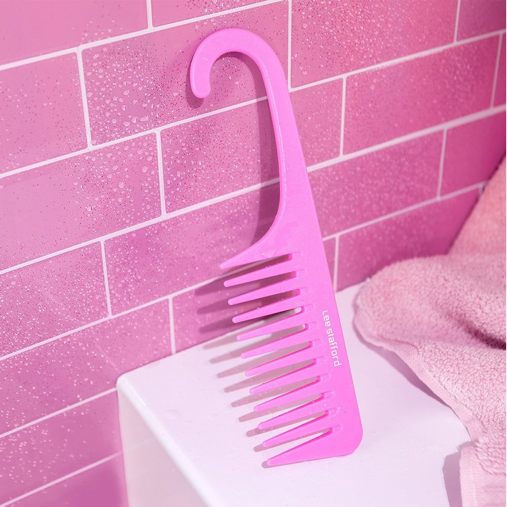 Een roze kam met brede tanden hangend aan een betegelde muur.