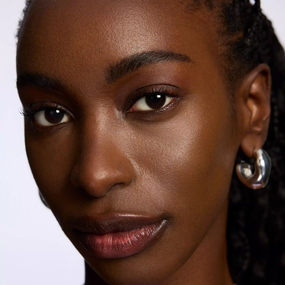 Gros plan d'un visage. Peau foncée, sourcils foncés. Boucles d'oreilles argentées.