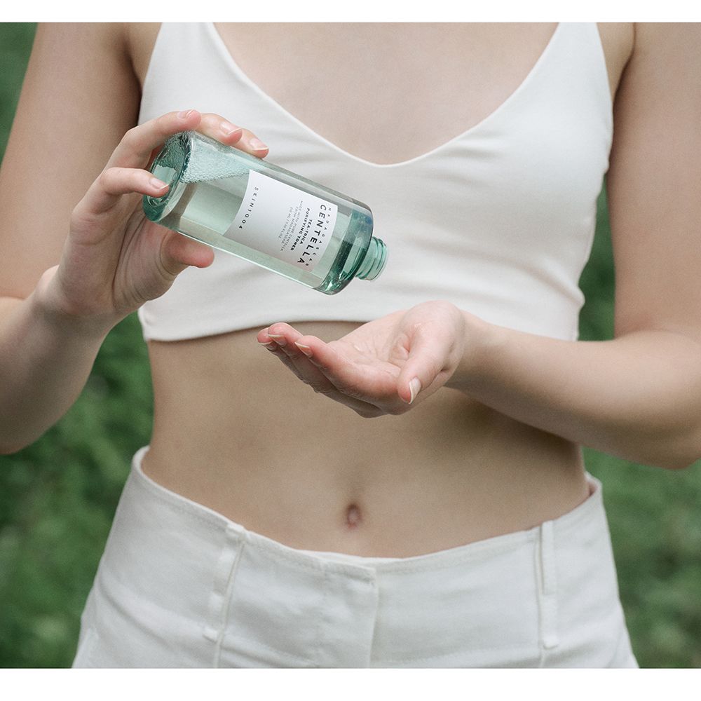 Persoon houdt een groene fles vast. Fles met witte dop. Opschrift: MADAGASCAR CENTELLA. Merk: SKIN1004.