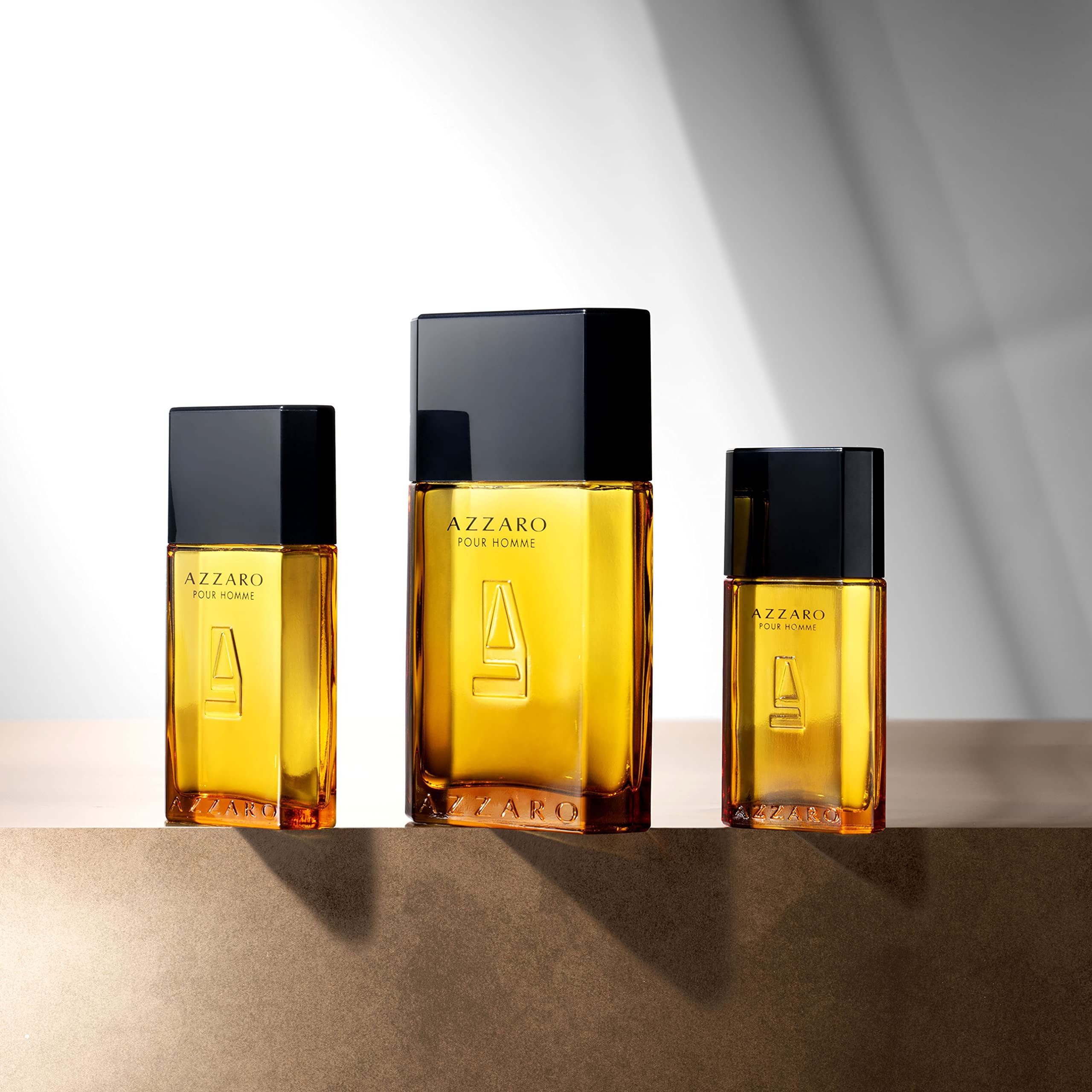 Trois flacons de parfum Azzaro Pour Homme de tailles différentes, contenant un liquide doré et surmontés de capuchons noirs.