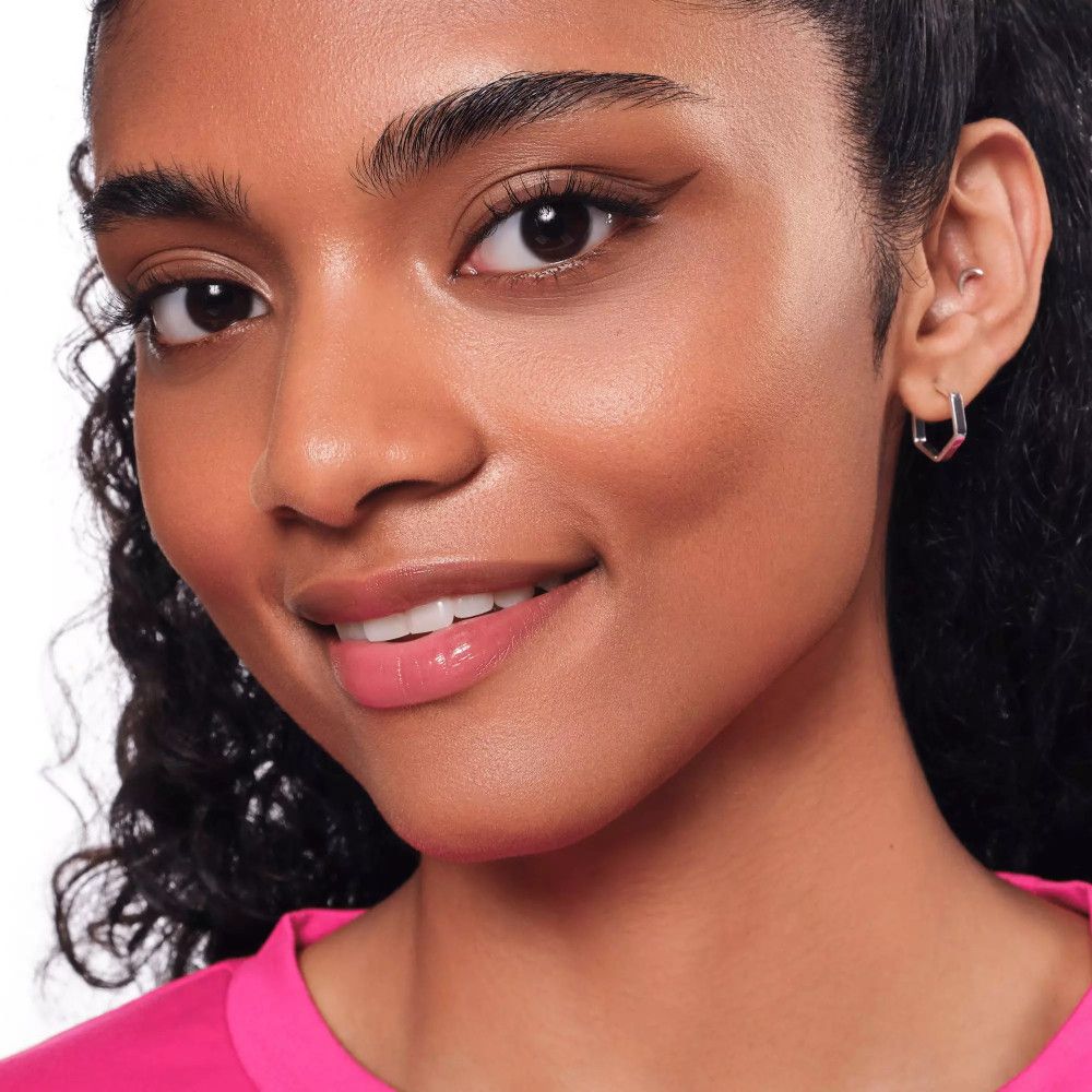 Portrait d'une femme souriante avec de l'eyeliner. Elle porte un haut rose.