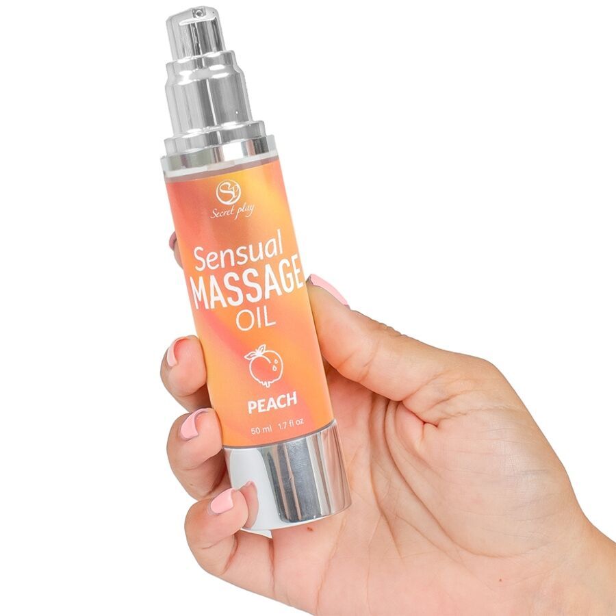 Fles massageolie, vastgehouden door een hand. Opschrift: Sensual Massage Oil Peach. Zilveren pompkop.