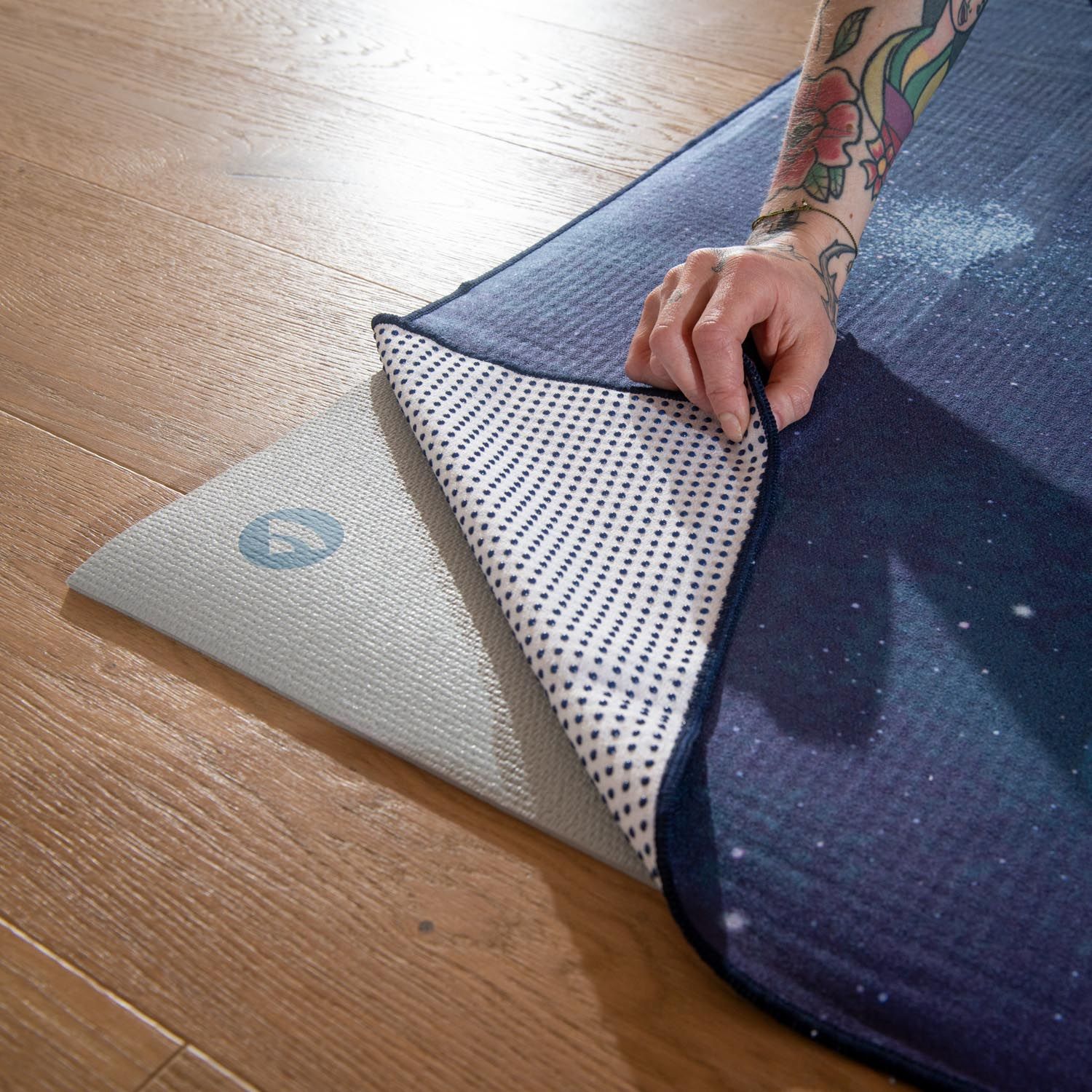 Een hand legt een yogamat met sterrenpatroon op een yogamat met noppenstructuur op de vloer.