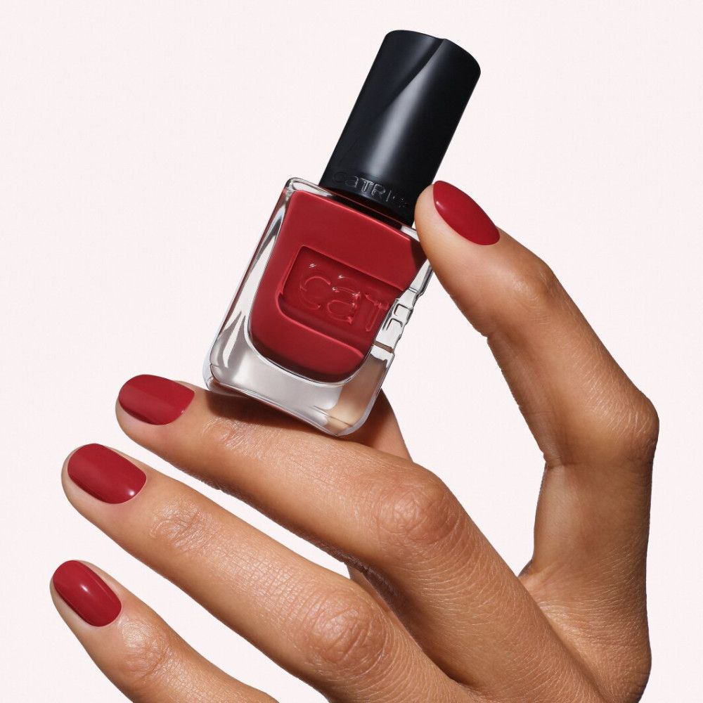 Bouteille de vernis à ongles rouge avec capuchon noir, tenue par une main aux ongles vernis.