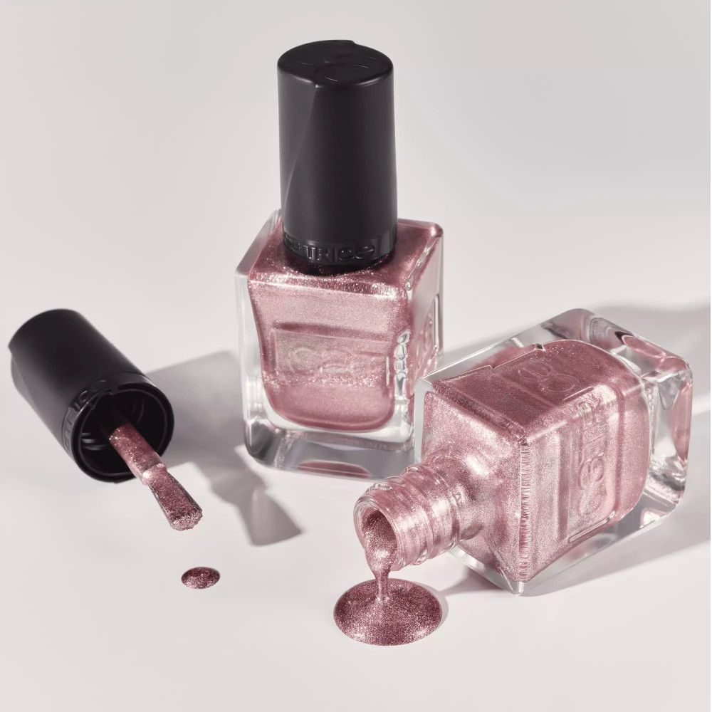 Trois flacons de vernis à ongles. Couleur rose scintillant. Un flacon ouvert, le vernis coule. Inscription "catrice" sur les flacons.
