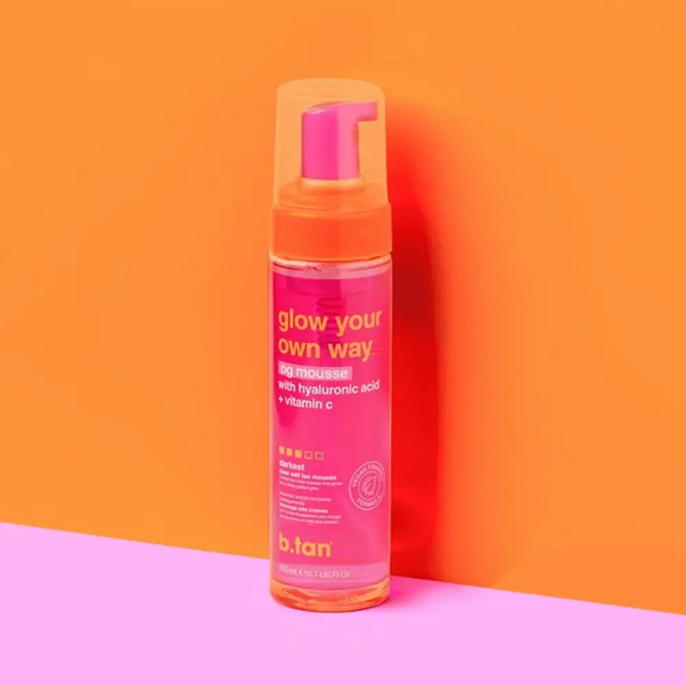 Flacon rose avec pompe. Inscription : glow your own way, the og mousse, avec acide hyaluronique + vitamine C. Marque : b.tan.
