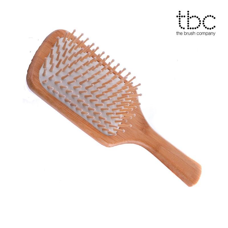Houten haarborstel met logo 'tbc the brush company', rechthoekige kop, houten pinnen op wit kussen.