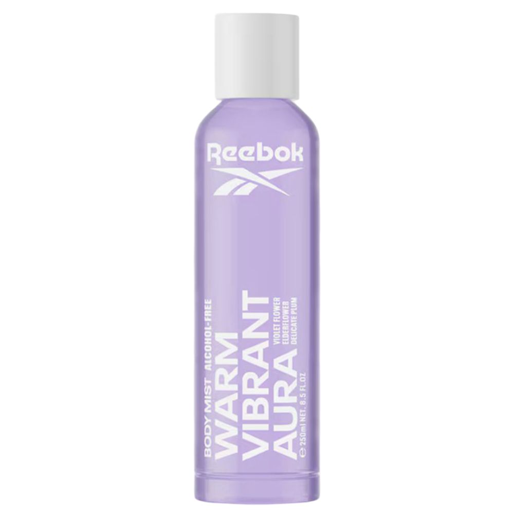 Spray corporel violet avec bouchon blanc. Texte: Warm Vibrant Aura, sans alcool. Marque: Reebok. Bouteille debout.