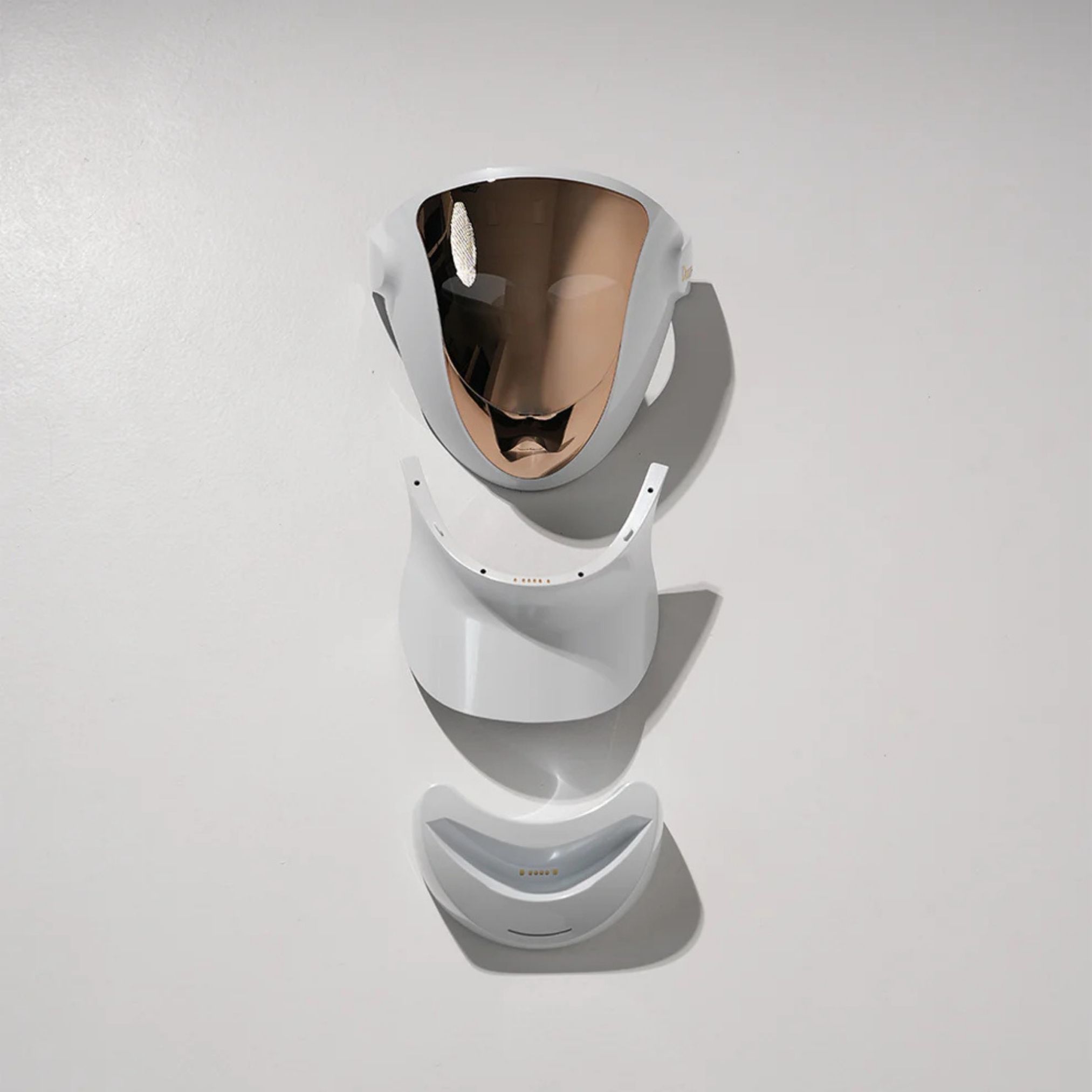 Gedemonteerd gezichtsmasker. Witte behuizing met gouden oppervlak. Bestaat uit drie delen: masker, nekverlenging, kin.