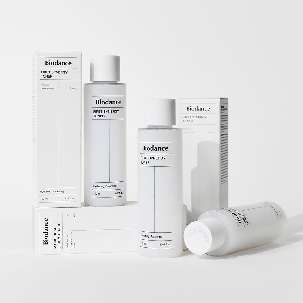 Plusieurs flacons et emballages. Inscription : Biodance First Synergy Toner. Emballage avec texte.
