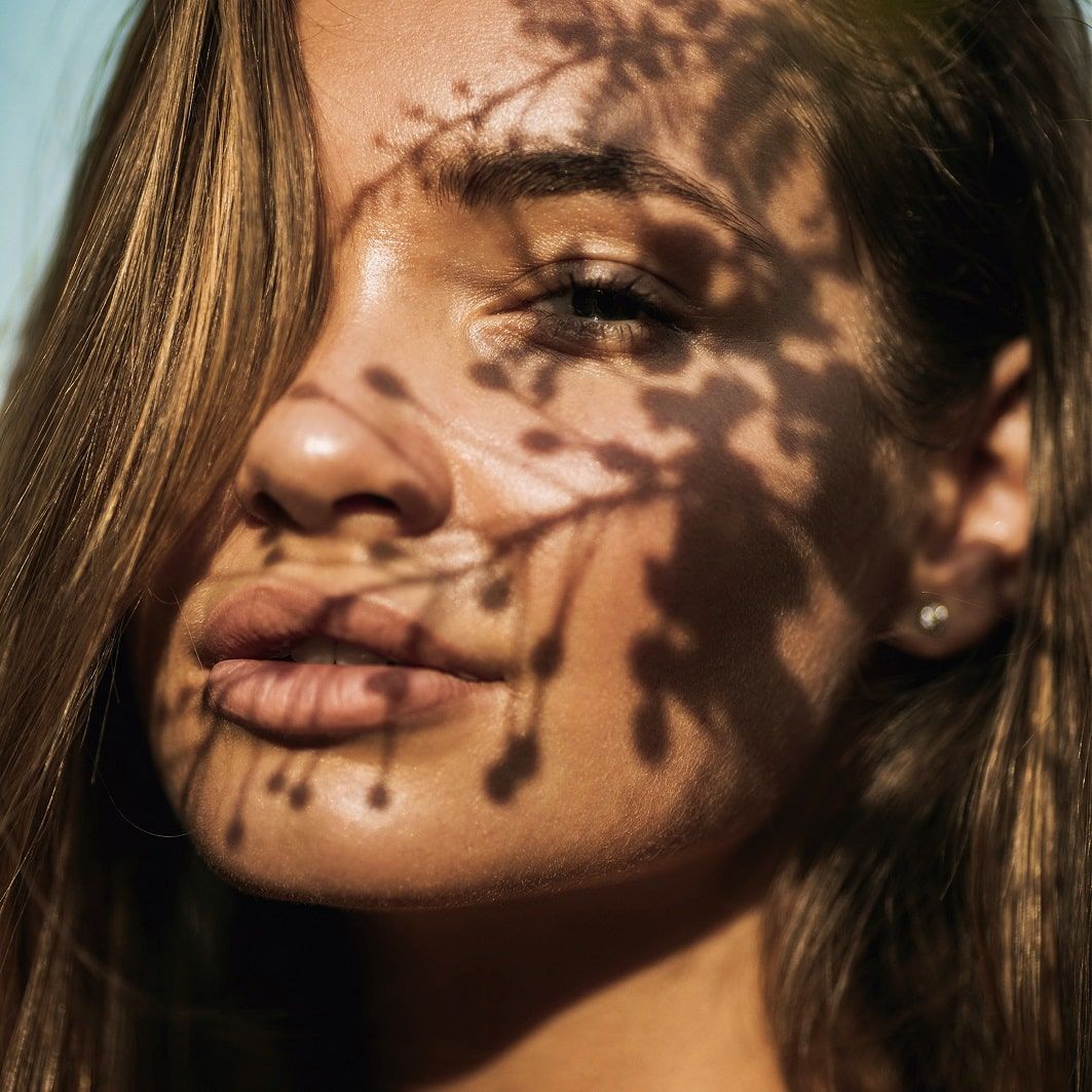 Gros plan d'un visage avec des ombres de feuilles. Peau avec exposition au soleil.