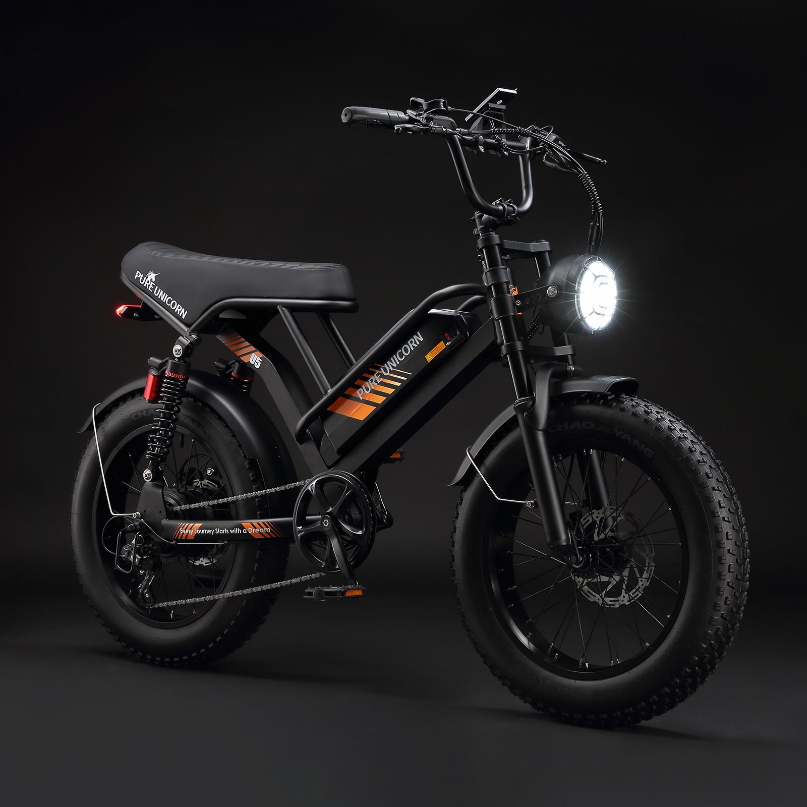 Zwarte elektrische fiets met brede banden, oranje accenten en PURE UNICORN. Koplamp brandt.