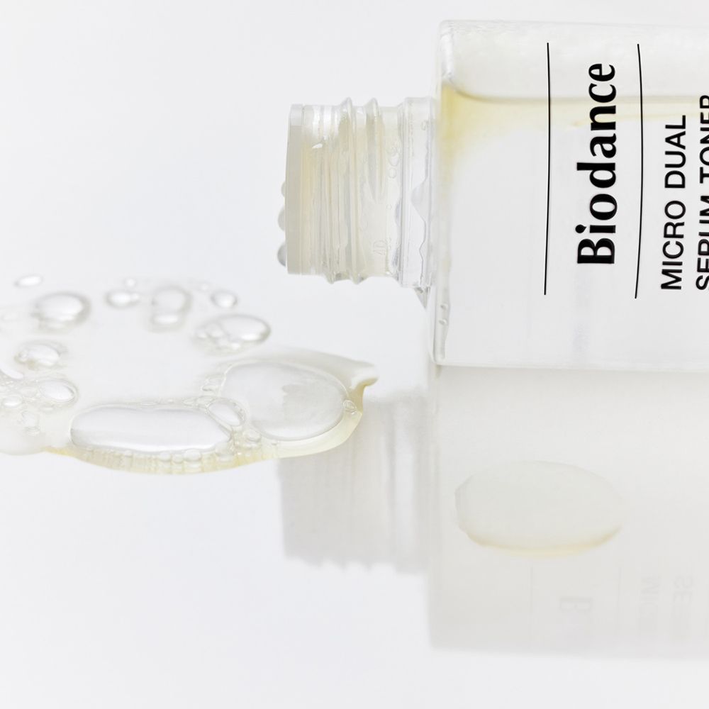 Transparante fles ligt. Opschrift: BIODANCE Micro Dual Serum Toner. Vloeistof en druppels ernaast.