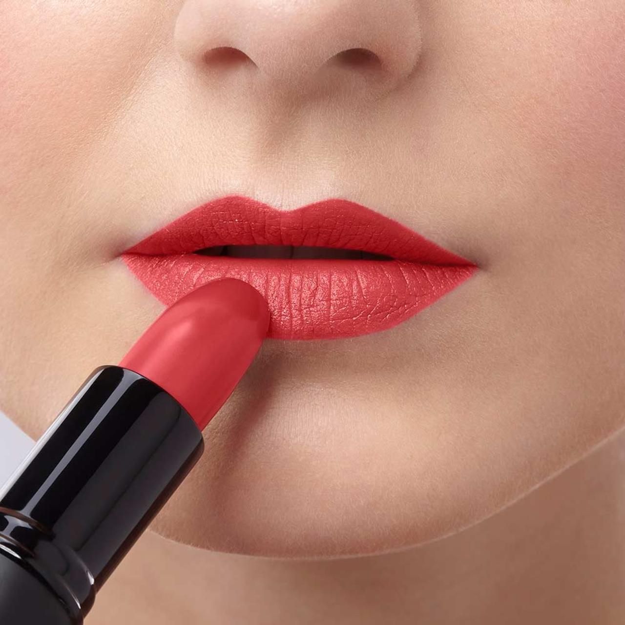 Personne appliquant du rouge à lèvres rouge sur les lèvres. Rouge à lèvres en étui noir.